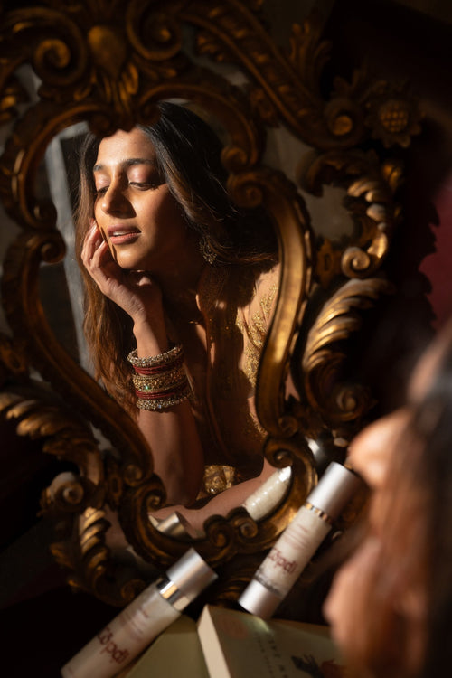 Woman examining her skin in a mirror while checking if her skincare is pregnancy-safe.